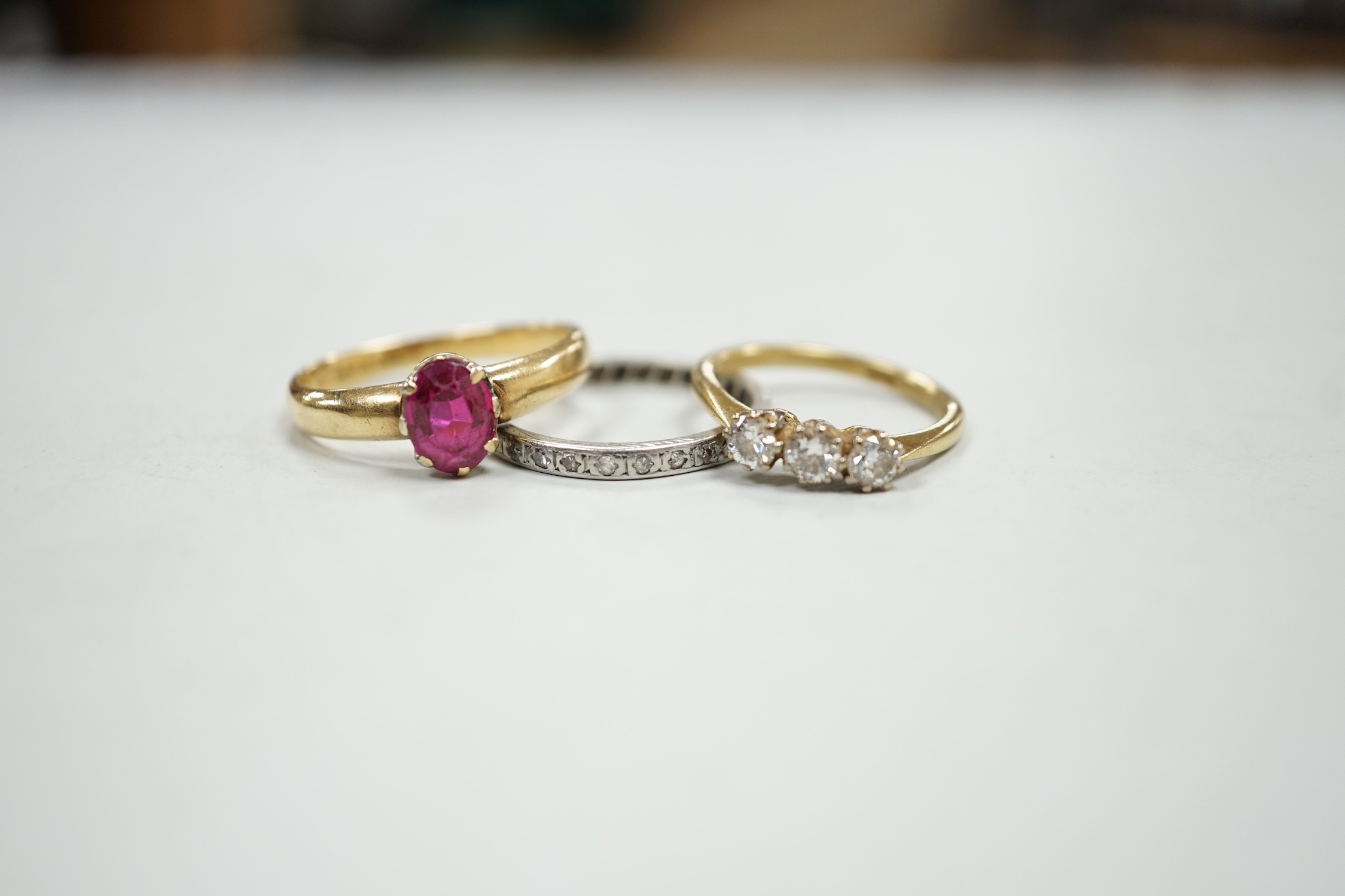 An 18ct and solitaire synthetic? ruby set ring, an 18ct and three stone diamond ring and a white metal and diamond chip set full eternity ring, gross weight 10.9 grams.